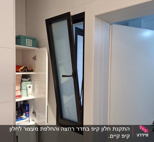חלון אלומיניום פתוח בחדר אמבטיה עם ארון פתוח.